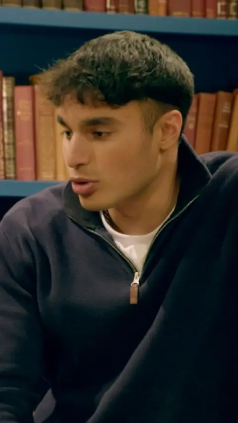 Faraaz from The Traitors in front of a book shelf