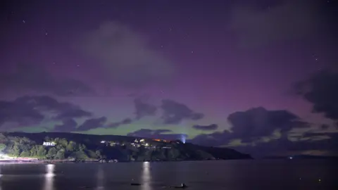 Urban Fox Hills sit to the right of a cove, a purple green glow from the northern lights dominates the top half of the frame