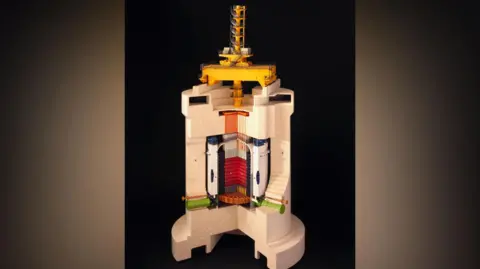 Getty Images A cross-section of a cylindrical, cream coloured structure about 20 poles running down it, representing the graphite bricks of the core. There is a yellow spiral structure at the top.