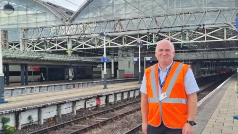 Northern A man in a orange high-vis jacket standing on a platform at Leeds Station