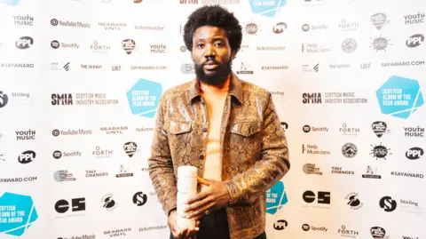 Scottish Album of the Year Alloysious Massaquoi holding a totem