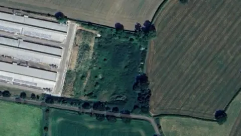 A photo showing a handful of fields of different colours, with buildings on the left of the image.
