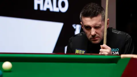 Getty Images A man squints at a white snooker ball from behind a snooker table.