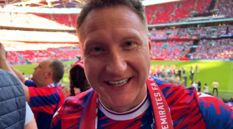 A Crystal Palace fan in a club t-shirt smiles at the camera