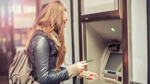 Getty Images Young woman withdrawing cash from atm