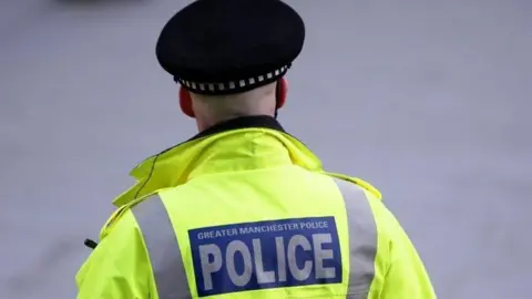 A Greater Manchester Police officer in uniform stands with his back to the camera