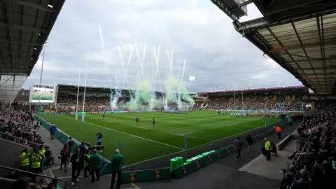 PA Media Spectators in stands on four sides of a rugby ground. Teams are walked out and smoke is billowing on one side of the pitch.