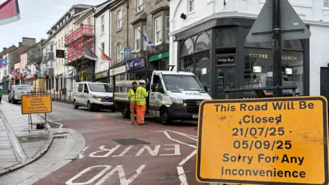 Yellow road signs in the front rightwarning of closures at the entrance to Market Jew Street in Penzance to the lk