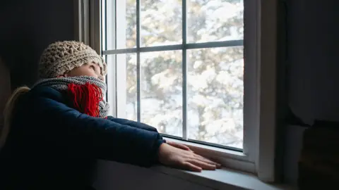Getty Images Girl looks out of window on cold day