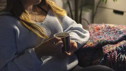 Getty Images A lady on a sofa holding a mug of tea