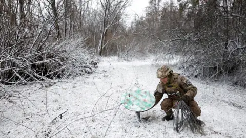 Reuters El soldado ucraniano se agacha para desconectar el receptor Starlink en la limpieza de bosques cubiertos de nieve en la línea de primera línea en enero de 2023