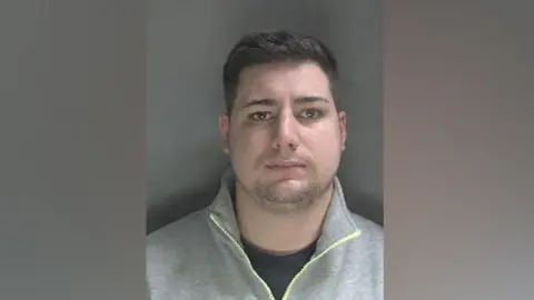 Bedfordshire Police James Barrett Barnett with short dark hair a black t-shirt and a grey zip-up sweater