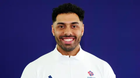 PA Leon Greenwood smiles at the camera in a studio shot showing him in his white Team GB jersey. He has short black hair and a short beard.