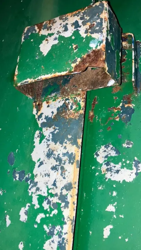 Shotton Steel RFC The green metal door of the storage container with no padlock. It is rusted.