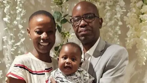 Handout A smiling woman holds a baby next to a man in glasses. They all look at the camera