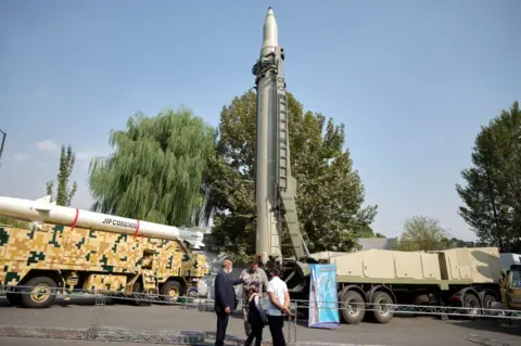 NurPhoto An Iranian family speaks with a member of the Islamic Revolution Guard Corps (IRGC) as they stand in front of a Qiam short-range ballistic missile, while visiting the Holy Defene Garden Museum in Tehran on 29 September 2020