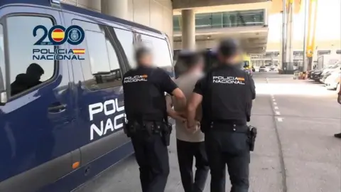 X/Policia Nacional Steven Lyons being taken into the back of a police van at Madrid Barajas Airport.