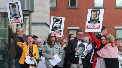 PA Media A crowd of people holding placards of their loved ones above their heads, are seen cheering and hugging.