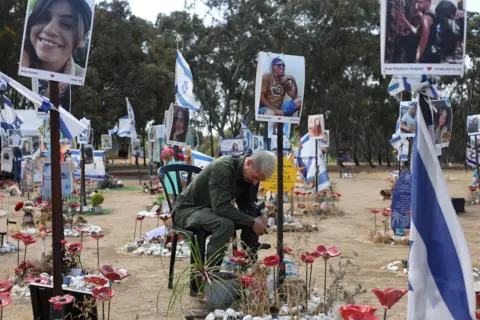 EPA A man sitting on a chair at the memorial site where the Nova music festival attack took place - he is surrounded by Israeli flags and pictures of people who were killed