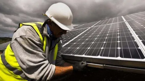 Worker in high viz yellow vest and white hard hat repairs a large solar panel