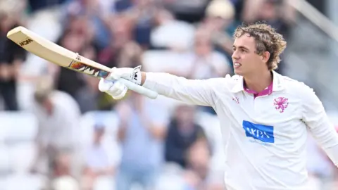Josh Thomas has his helmet off and points his bat towards the dressing room after scoring a century for Somerset