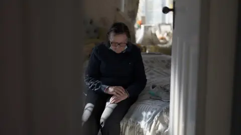 Jo sits on a bed looking down at her hands