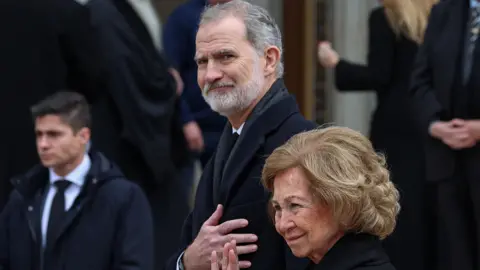 Reuters Spain's King Felipe and his mother, Queen Sofía, leaving the funeral of Princess Irene of Greece and Denmark in Athens, Greece in January 2026. They are wearing black, and the king is holding his hand over his heart while his mother in front of his, is waving.