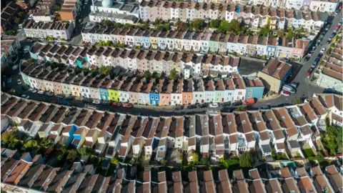 Getty Images An aerial view of terraced streets in Bristol, UK. Seven streets of homes, arranged in a uniform pattern, are broken up only by roads linking them. The streets are colourful, with houses on each painted different colours. There are a range of neutral and pastel shades on display, with one lime green frontage drawing particular attention. The angle of the plentiful parked cars tells the viewer that the streets are on a hill. It's a heavily residential area, with only one building - a white, domed mosque - towards the rear of the photo that appears to serve another purpose.