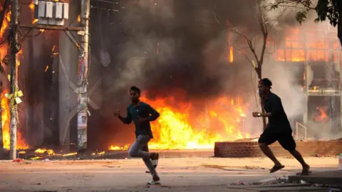 Getty Images Dua pria berlari di jalan. Di belakang mereka ada toko terbakar.