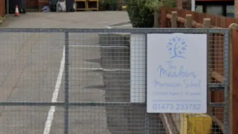 Google Maps A Google Maps street view image of the entrance of The Meadows Montessori School. A metal fence with a sign for the school restricts access to a small road which leads to the site. 