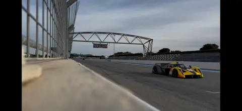 Kirsty Peters A yellow prototype sports car going down the straight of the Paul Ricard circuit.