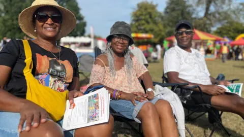 Jon Wright/BBC Sharon Marston, Joy Smith and Michael Lythcott sit on camping chairs in the sunshine at the multicultural festival