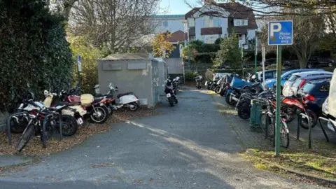 The motorcycle area of the Odeon carpark. It shows bikes parked along the sides of the area with housing in the background
Copyright