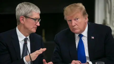 Tim Cook speaks to Donald Trump while sitting around a table at a 2019 workforce advisory board meeting