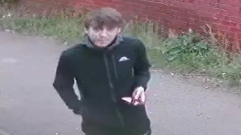 A still image of CCTV footage taken of a man with short brown hair, black jacket 