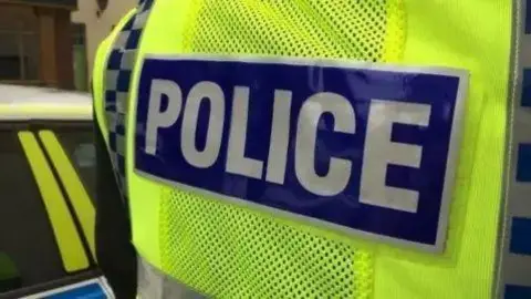 The back of a police officer's jacket as they stand next to a police car. 
