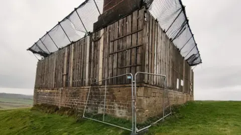 Wooden fences and metal fences surround the base of the monument