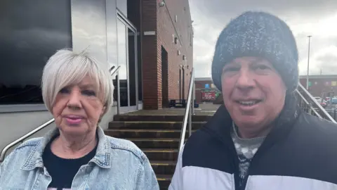 Elizabeth Scott, with blonde hair and denim jacket, alongside Bill Scott wearing hat and black and grey jacket