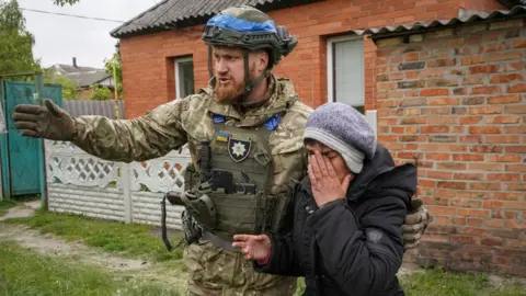 Ukrainian soldier in uniform helping a woman in tears evacuate from village in Kharkiv