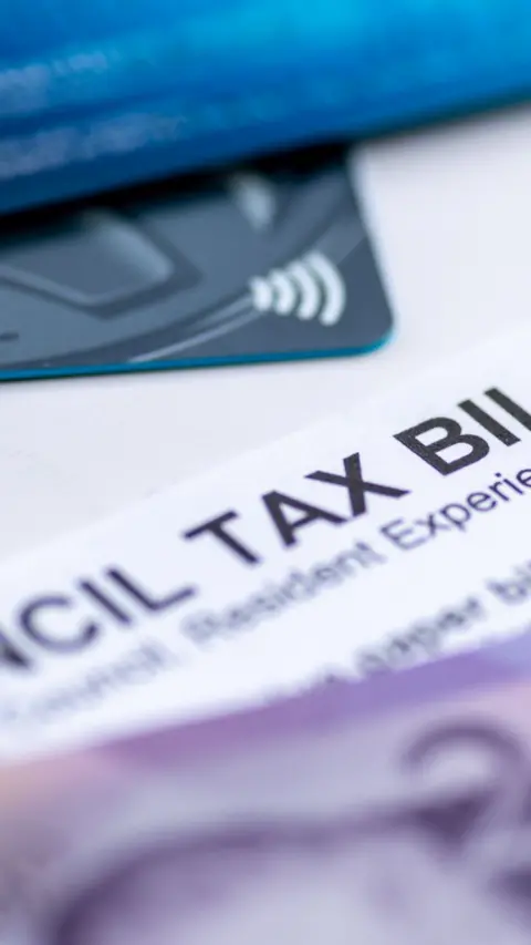 A Council Tax Bill in between Pound Sterling bank notes and bank payment cards.