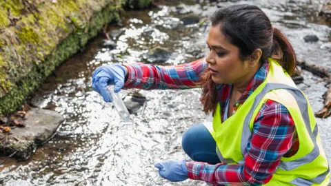 Getty Images  Woman takes water sample from a river 
