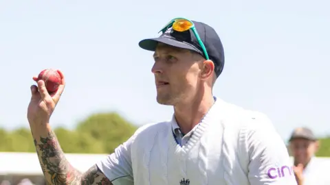 Brydon Carse walking off the field, with the ball in his hand to acknowledge taking six wickets against New Zealand