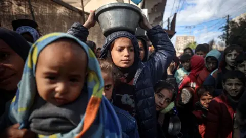 Shutterstock Displaced Palestinian children wait in a line whilst holding bowls as they wait to receive a free hot meal in Deir al-Balah, central Gaza Strip, on 26 November 2024