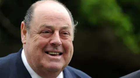 A balding man wearing a blue suit and white shirt.
