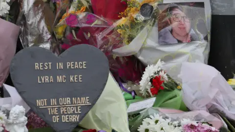 PA Media Flowers left at the scene of Lyra McKee's murder. They include a heart that says rest in peace Lyra McKee, not in our name, the people of Derry. There is also a picture of Lyra.