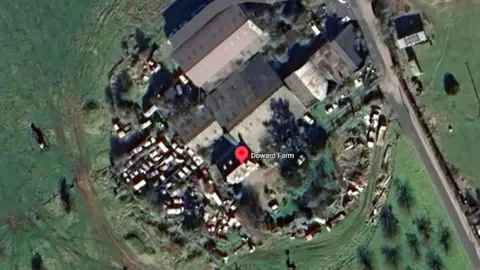 Google An aerial view of a farm with lots of cars parked outside it.