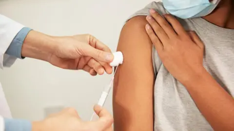 Getty Images A doctor gives an injection to a patient who has rolled up their sleeve. 