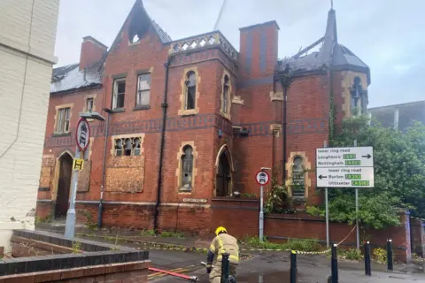 Derbyshire Fire and Rescue Service A cordon around a burning building with a firefighter working on a hose connection