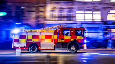 A fire engine drives on an urban road at night with blue lights on.