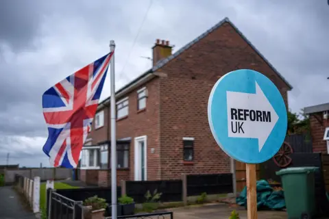 Getty Images A light blue Reform UK placard next to a Union Jack outside a house.